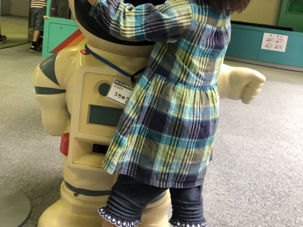 宇宙服を着たオブジェに抱きつく女児